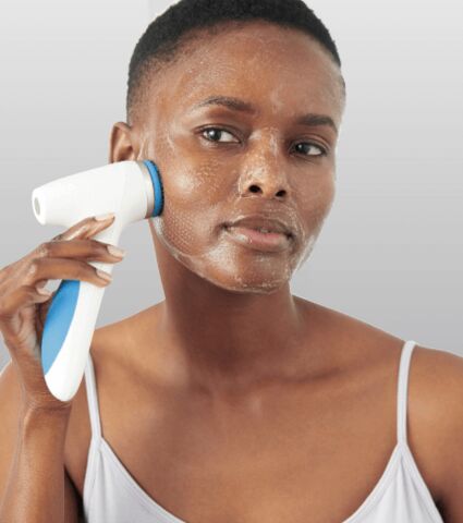 Woman cleansing her face with LumiSpa iO beauty device.