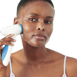 A woman cleansing her face with the LumiSpa iO device and LumiSpa treatment cleanser for dry skin.