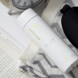 A bottle of ageLOC Youth Supplements lying on a folded blanket next to a clock and an open book.