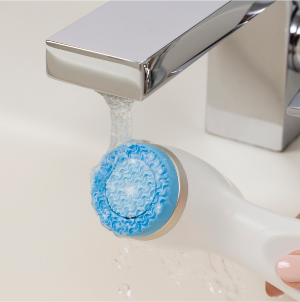 A woman's hand wetting the ageLOC LumiSpa oi device in a bathroom sink. 