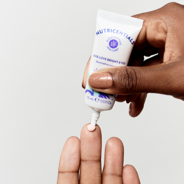 A woman's hands adding a small drop of Nutricentials Illuminating Eye Cream to her fingertip.