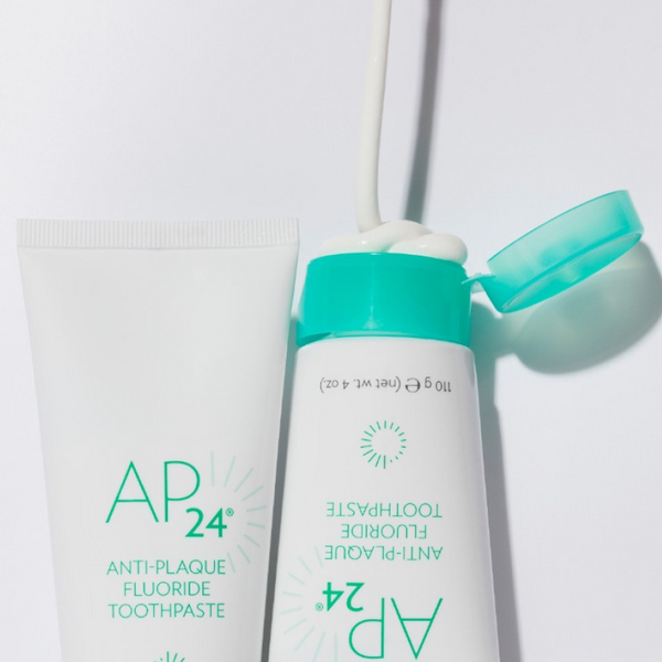 One open and one closed bottle of the Nu Skin AP 24 anti-plaque fluoride toothpaste on a white background.