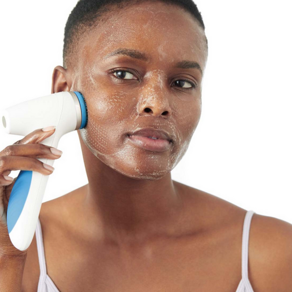 A woman cleansing her face with the LumiSpa iO device and LumiSpa treatment cleanser for dry skin.