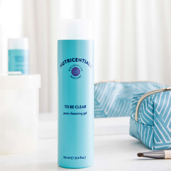 Nutricentials To Be Clear Pure Cleansing Gel displayed on a white marble countertop with makeup bag.